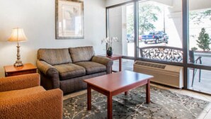 A living room with a sofa, a coffee table, a lamp, and a large window with a view of the street. - Quality Inn US65 & E. Battlefield Rd. Springfield (Springfield)