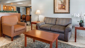 A lobby with a sofa, armchair, and a wooden coffee table. There is a framed picture on the wall and a vase with flowers on a side table. - Quality Inn US65 & E. Battlefield Rd. Springfield (Springfield)