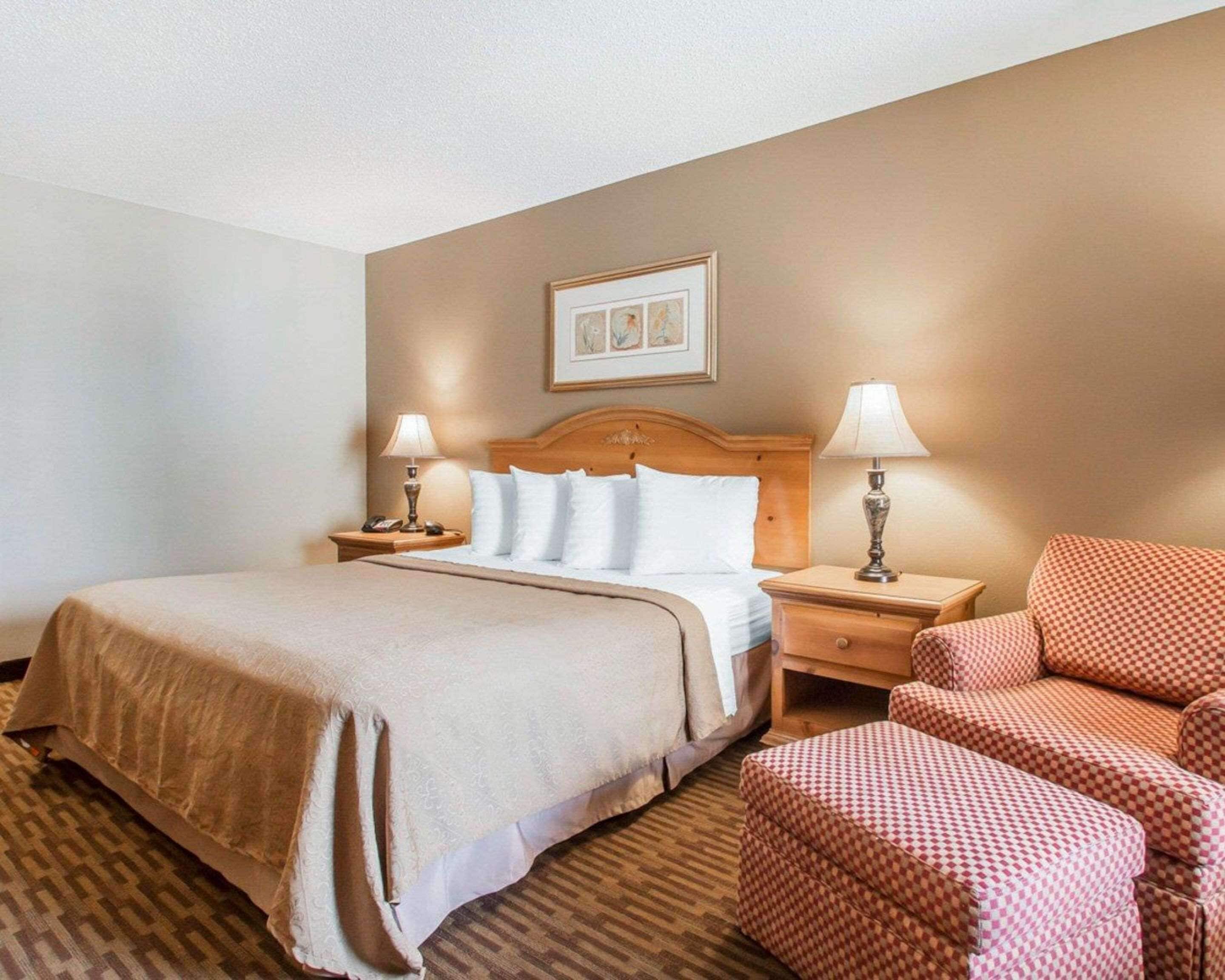 A hotel room with a large bed, two bedside tables with lamps, a checkered armchair, and a framed picture on the wall.