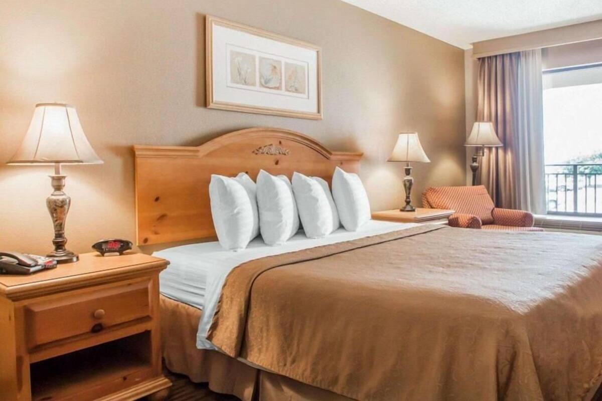 A hotel room with a bed, two bedside tables, a nightstand, a framed picture on the wall, and a window with curtains.