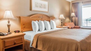 A hotel room with a large bed, two bedside tables, a nightstand, a framed picture on the wall, and a window with curtains. - Quality Inn US65 & E. Battlefield Rd. Springfield (Springfield)