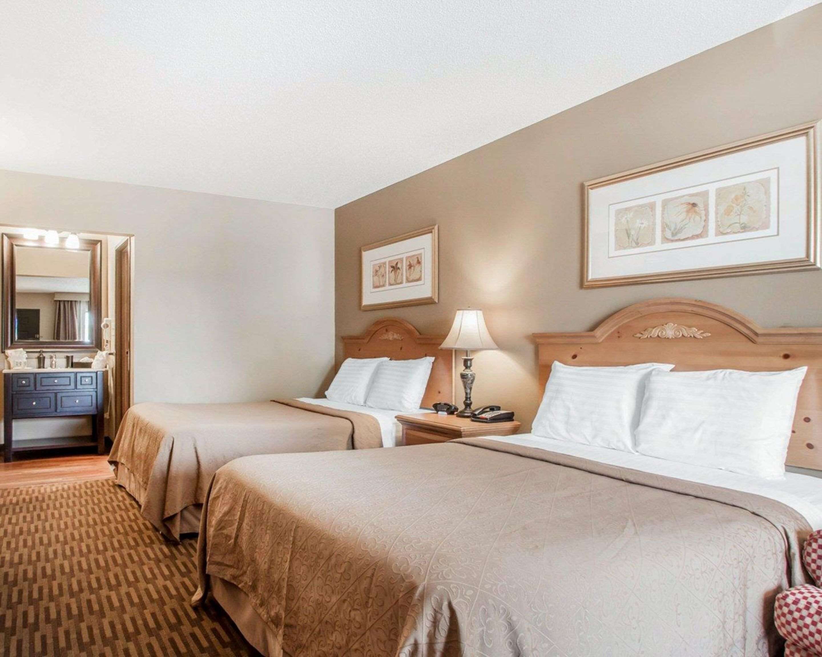 A hotel room with two beds, a dresser, a mirror, and framed artwork on the walls.