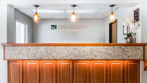 A reception desk with a marble top and wooden paneling, overhead pendant lighting, and a sign that reads "Quality Inn by Choice Hotel". - Quality Inn US65 & E. Battlefield Rd. Springfield (Springfield)