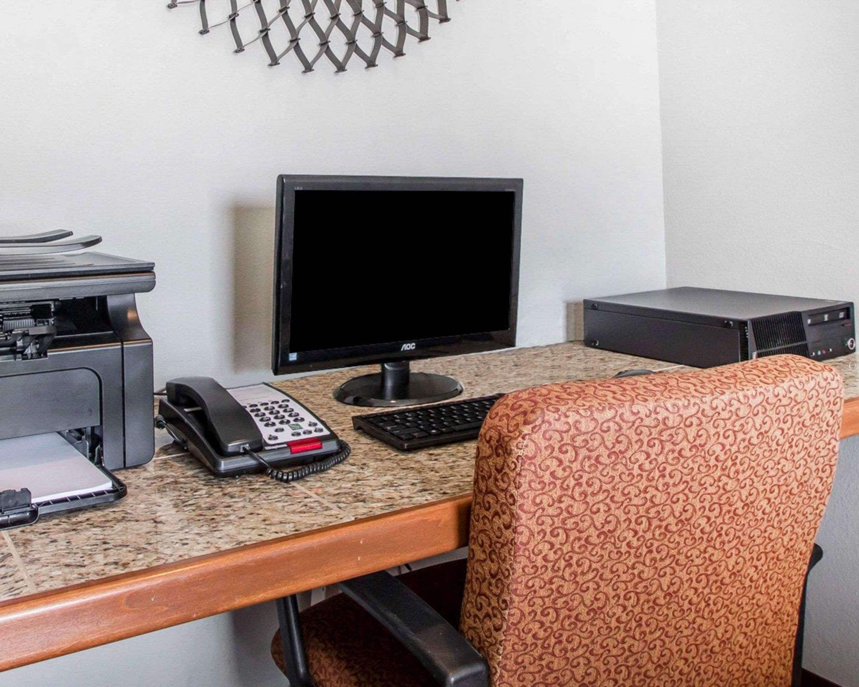 Ein Hotelzimmer mit Schreibtisch, Computermonitor, Drucker, Telefon und einem gemusterten Sessel.