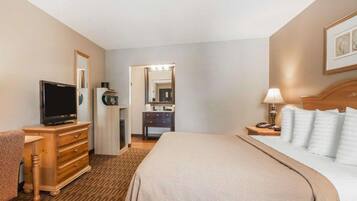 A hotel room with a bed, a TV, a desk, a dresser, a mirror, and a bathroom.
