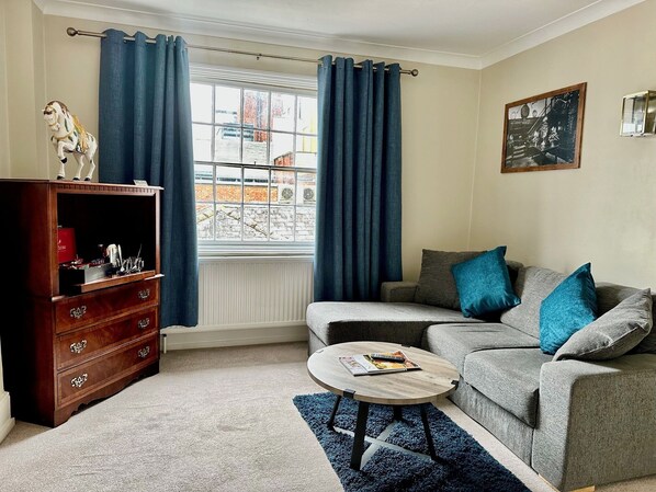 A living room with a sofa, a coffee table, a wooden cabinet, and a window with curtains. - Angel Hotel (Guildford)
