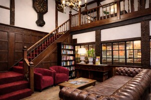 Una biblioteca con una escalera de madera, sillones rojos, un sofá de cuero y una estantería.