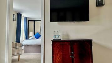 A hotel room with a bed, a television mounted on the wall, and a wooden cabinet with toiletries.