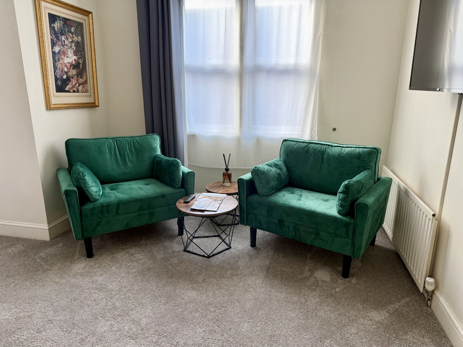 Une pièce avec deux canapés verts, une petite table ronde et un tableau accroché au mur.