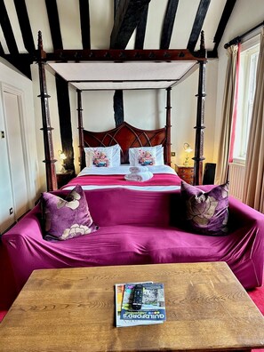 A four-poster canopy bed with floral pillows, a wooden coffee table with a magazine, and a view of the room's architecture. - Angel Hotel (Guildford)
