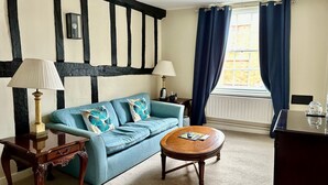 A room with a blue sofa, two lamps, a wooden coffee table, and a window with blue curtains. - Angel Hotel (Guildford)