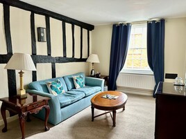 Una habitación con sofá azul, dos lámparas, una mesa de centro de madera y una ventana con cortinas azules.