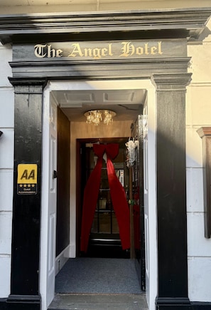The entrance to The Angel Hotel with a black and white facade, a gold sign above the door, and a red ribbon tied around the door frame.