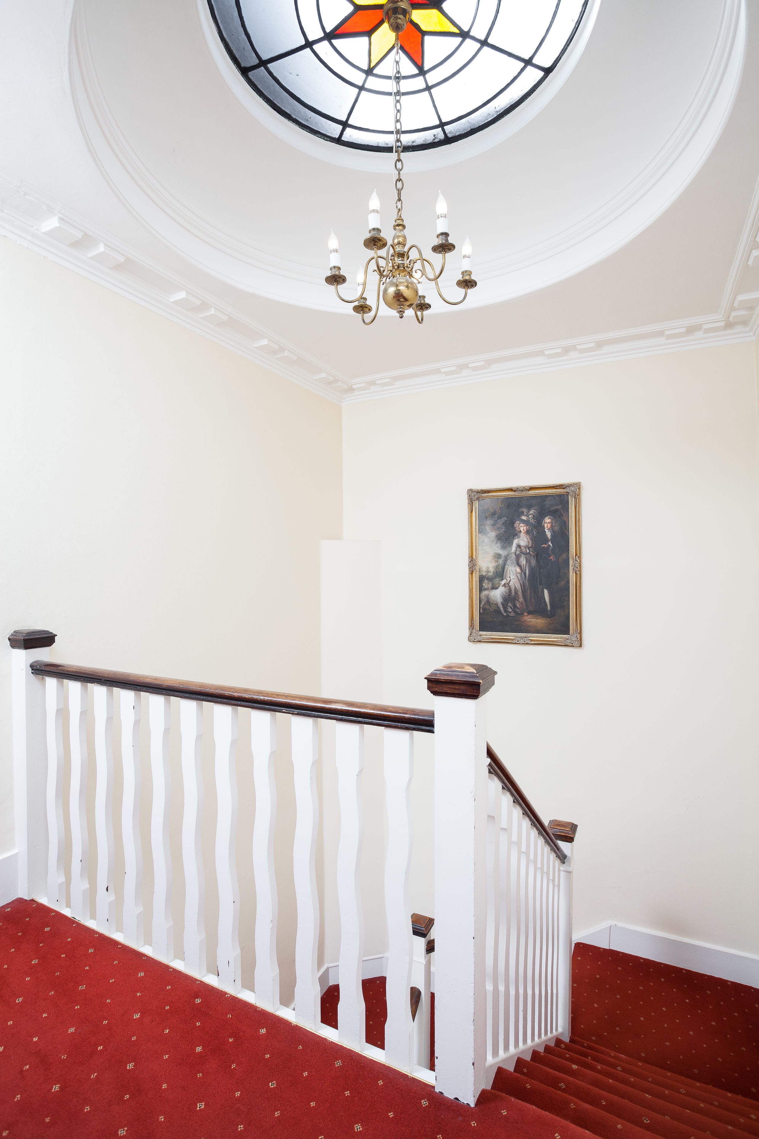 A staircase with a red carpet, white balustrade, and a chandelier.