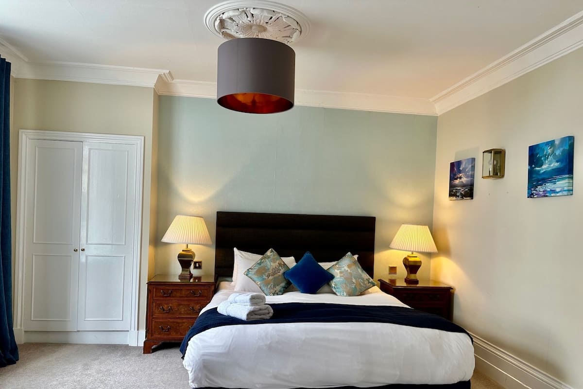 A neatly arranged bedroom with a large bed, two bedside tables with lamps, a door, and two wall-mounted paintings.