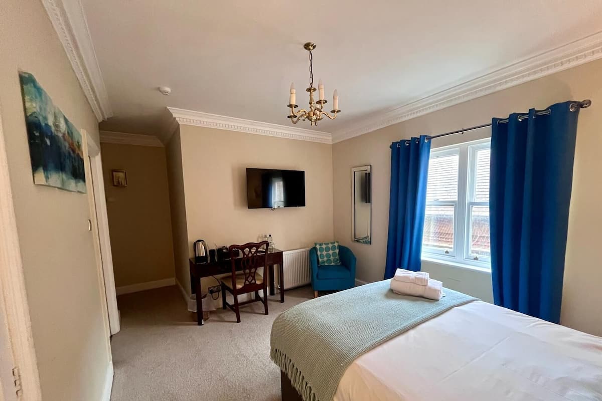 A hotel room with a bed, a desk with a chair, a television, and a window with curtains.
