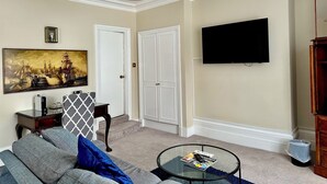 Una sala de estar con sofá, mesa de centro, cuadro, televisor y una puerta.