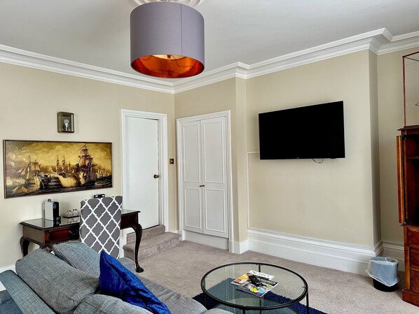 Una sala de estar con sofá, mesa de centro, cuadro, televisor y una puerta.
