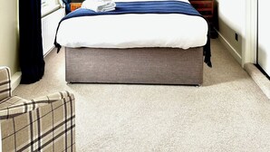 Un dormitorio ordenado con una cama grande, dos mesitas de noche con lámparas, una silla y una ventana con cortinas.