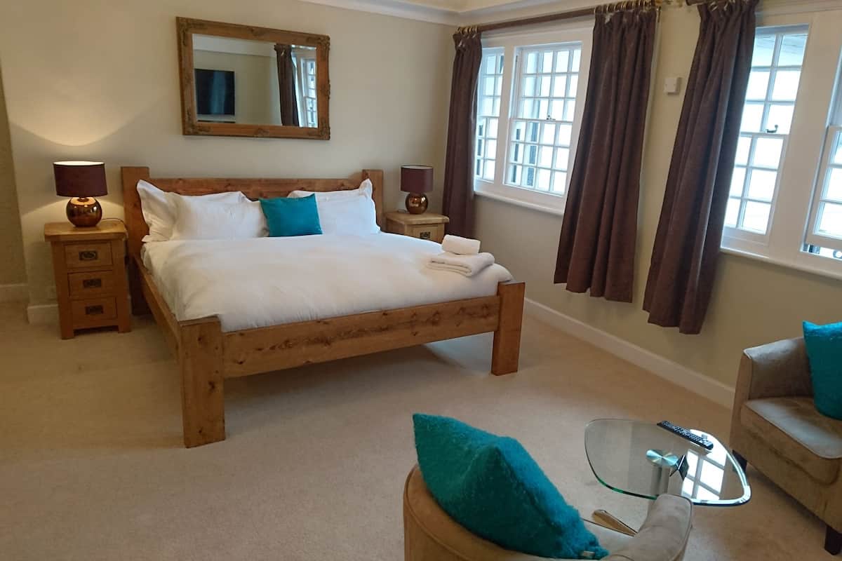 A bedroom with a wooden bed, two bedside tables, a glass coffee table, a chair, and a large window with curtains.
