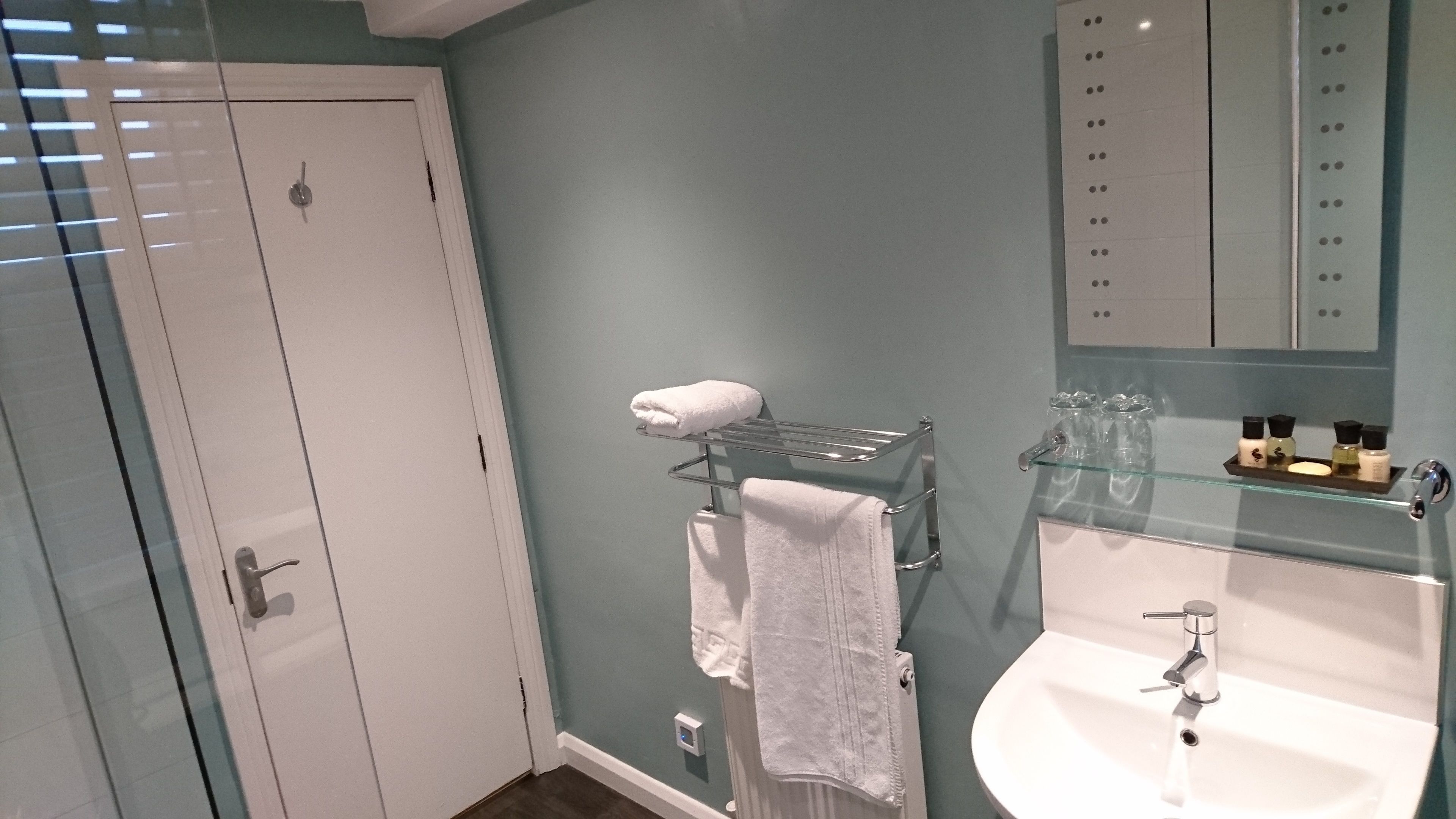 Casa de banho com cabine de chuveiro em vidro, uma sanita branca e um balcão de vidro com produtos de higiene pessoal.