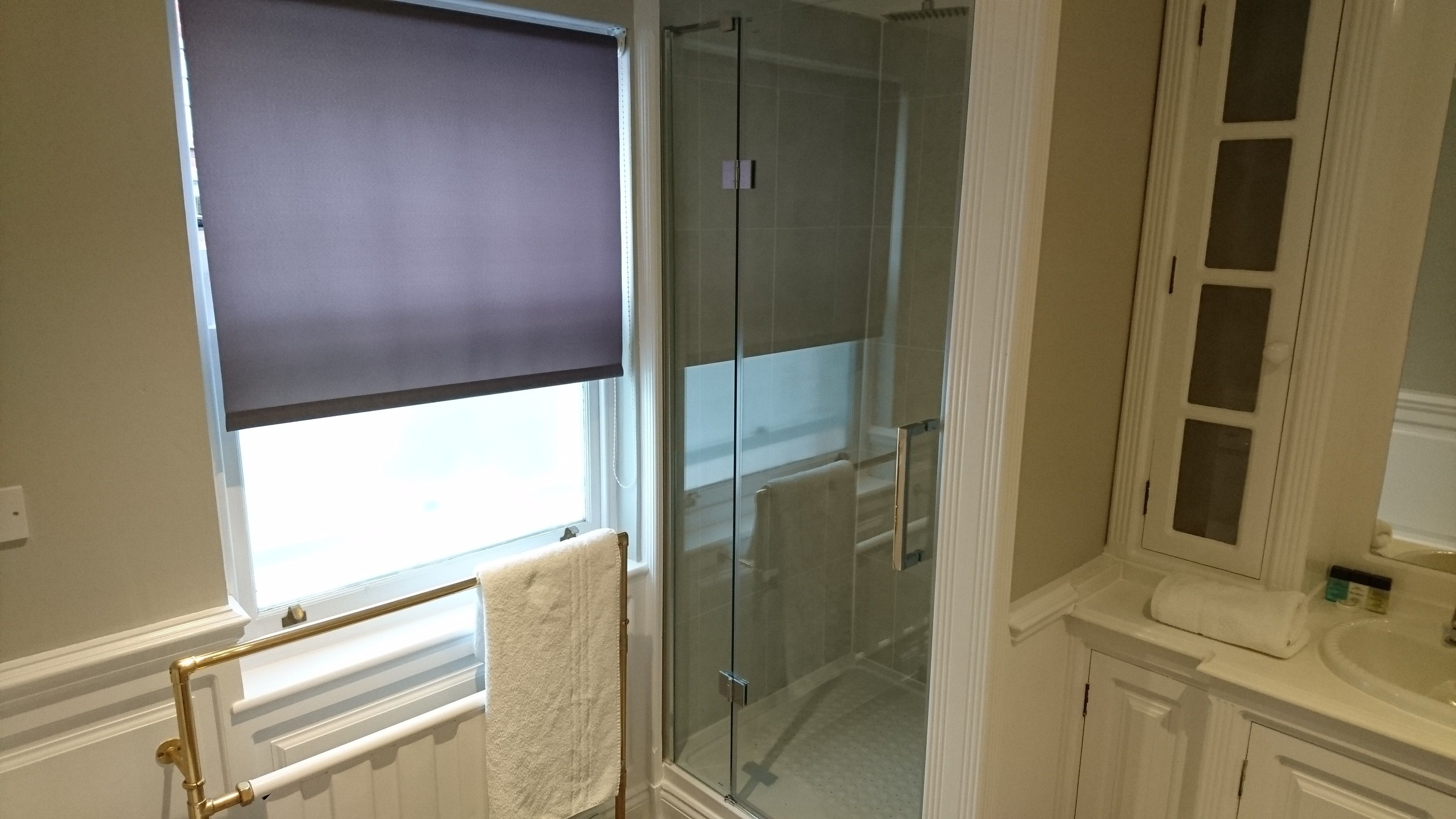 Un baño con cabina de ducha de vidrio, una ventana con persiana y un radiador blanco.