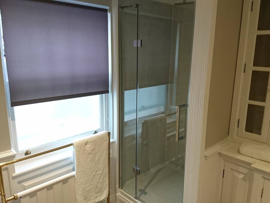 Un baño con cabina de ducha de vidrio, una ventana con persiana y un radiador blanco.
