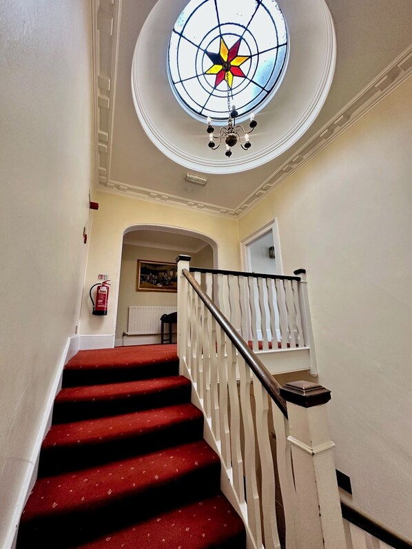 A staircase with red carpeted steps and white railings, leading to a room with a white door and a fire extinguisher on the wall.