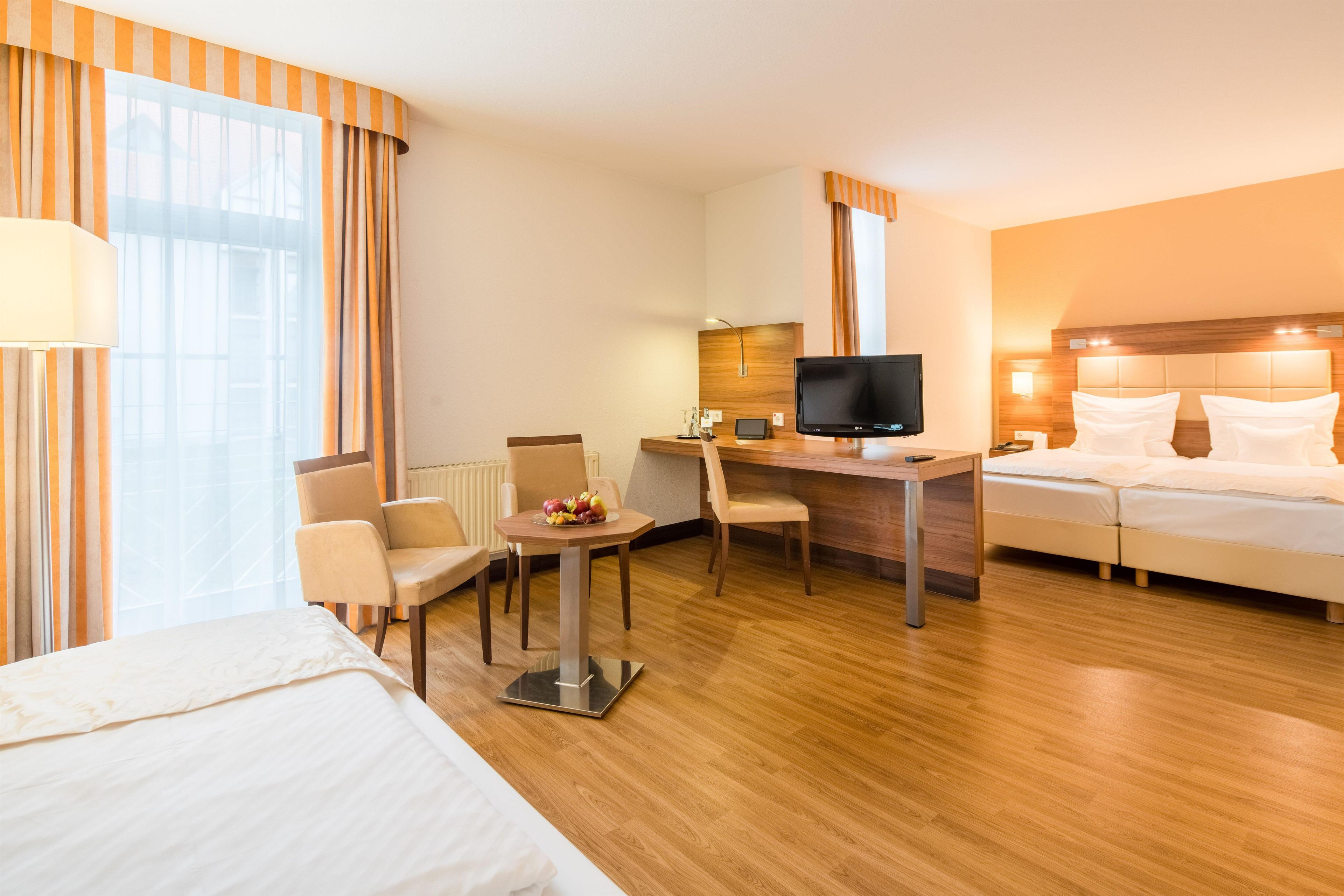 A hotel room with a bed, desk, chair, TV, and a small table with fruit.