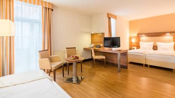 A hotel room with a bed, desk, chair, TV, and a small table with fruit.