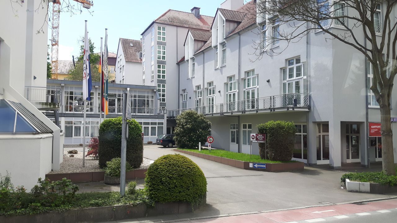 Un immeuble à plusieurs étages doté d’une entrée sécurisée par un portail, d’un espace de stationnement et d’un mât sur lequel sont hissés plusieurs drapeaux.