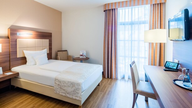 A hotel room with a bed, bedside table, lamp, chair, desk, and a TV. - Best Western Plus Hotel Am Schlossberg (Nuertingen)