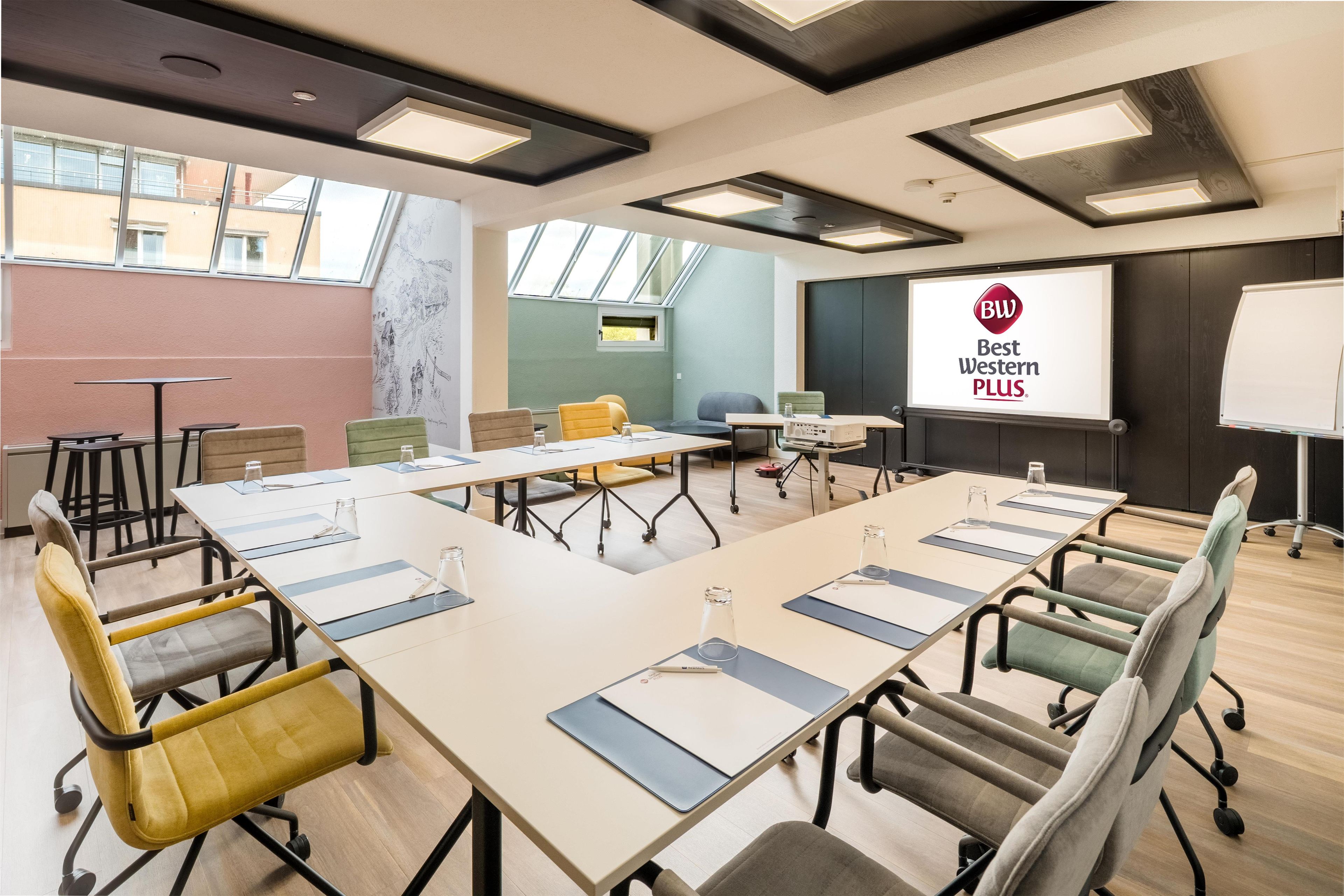 A conference room with a long table, multiple chairs, a projector screen, and a whiteboard.