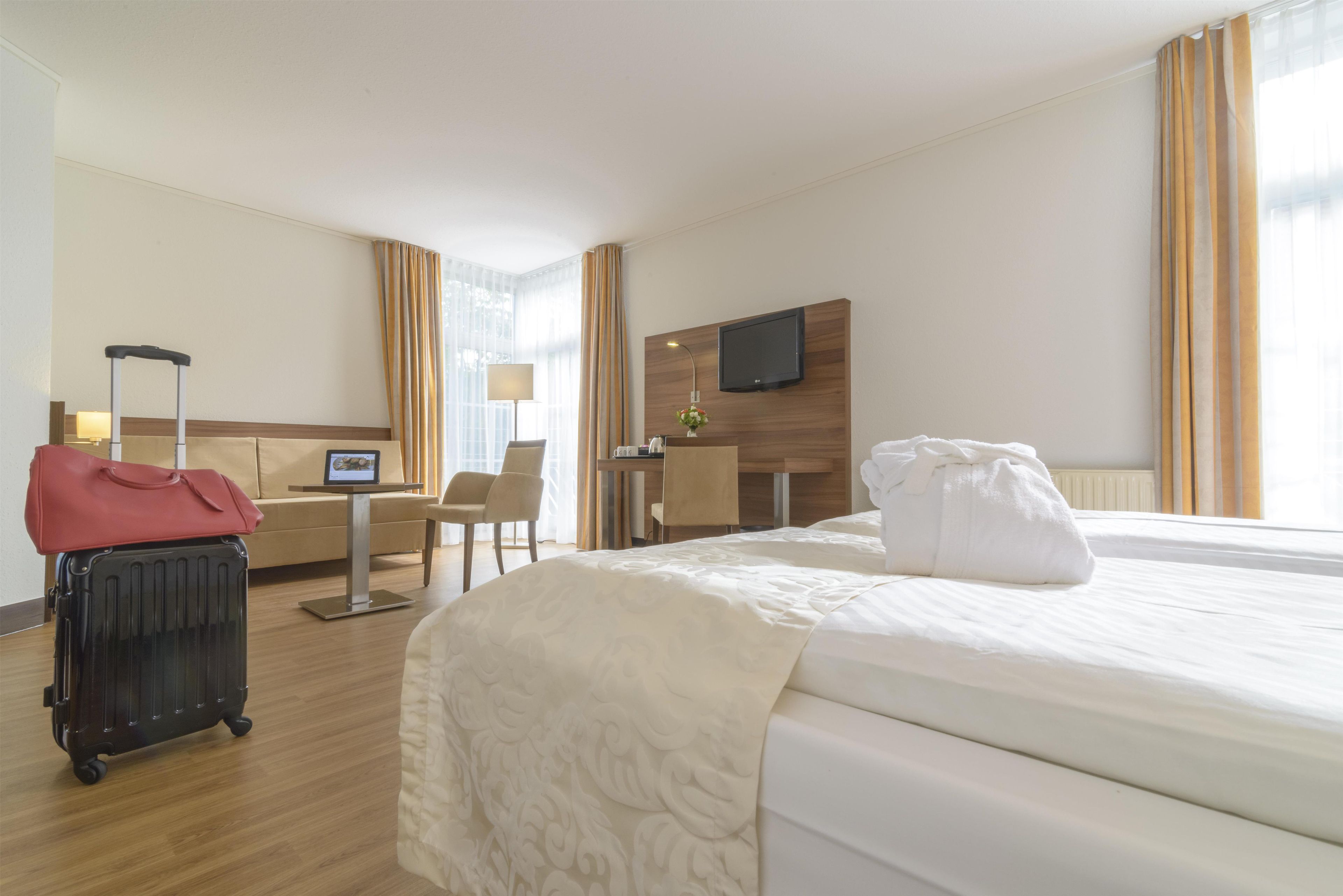 Une chambre d’hôtel avec un lit, un bureau, une chaise, une télévision et une valise.