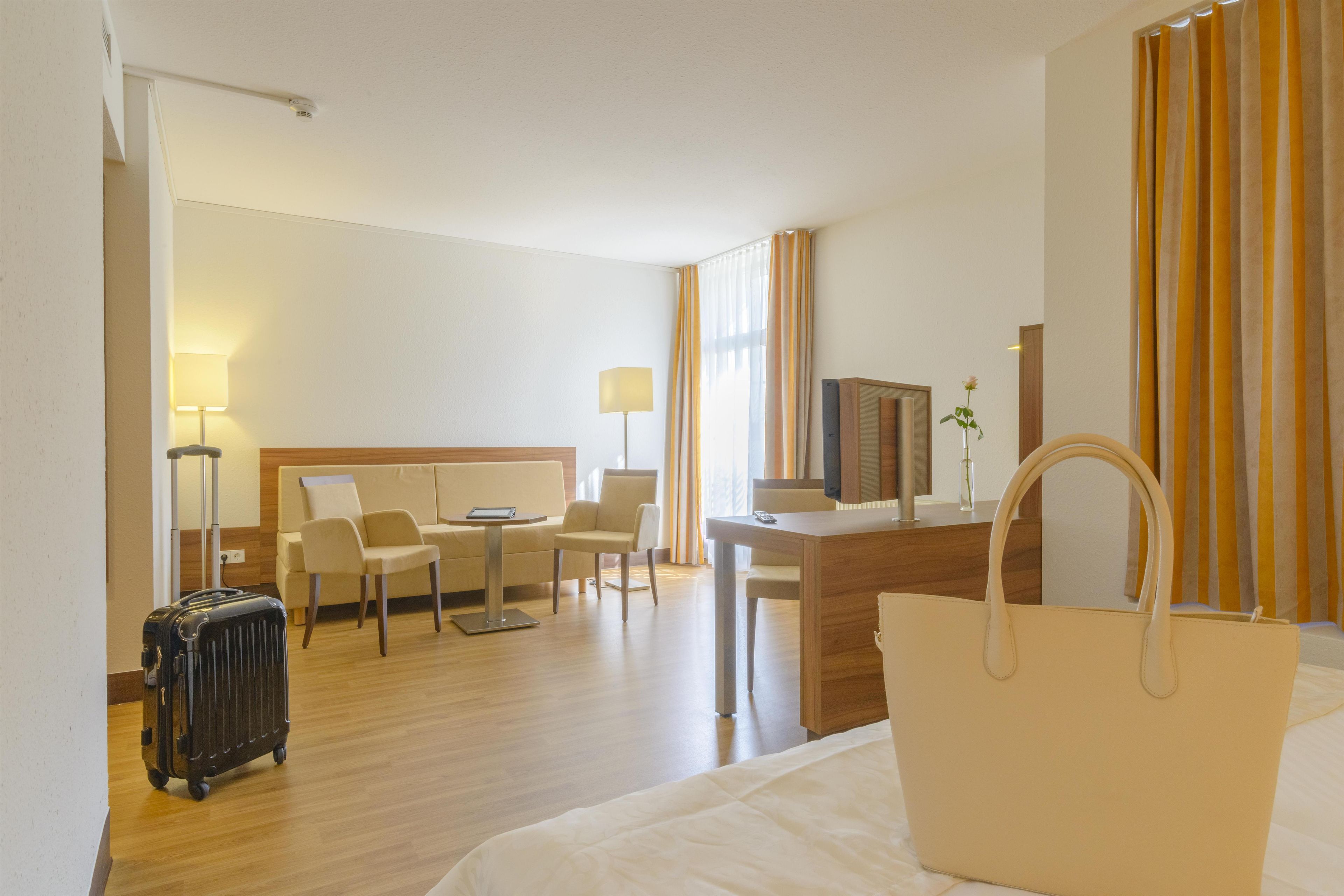 Een hotelkamer met een bed, een bureau, een stoel, een televisie, een lamp, een koffer en een handtas.