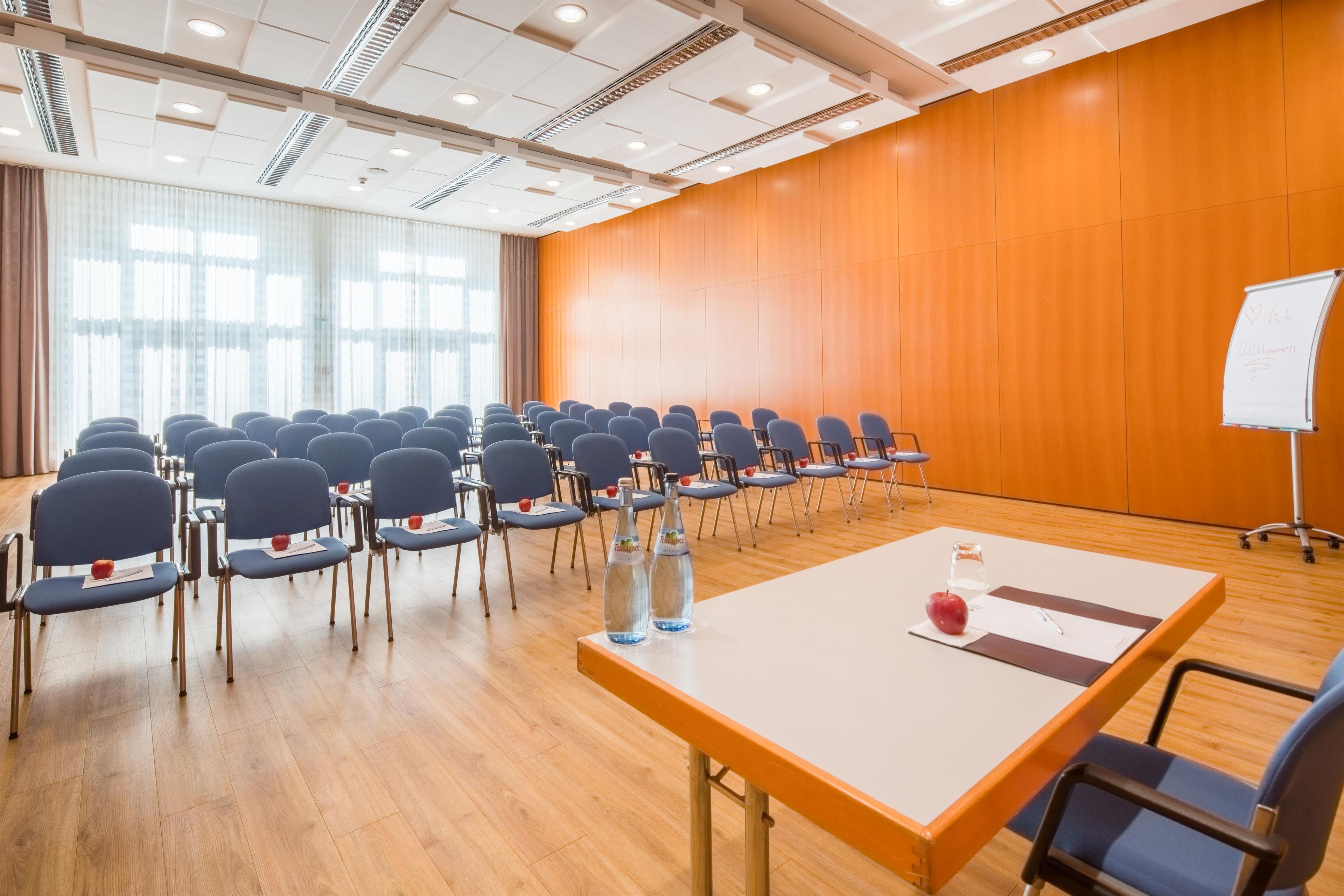 A conference room with rows of chairs, a whiteboard, and a table with water bottles and an apple.