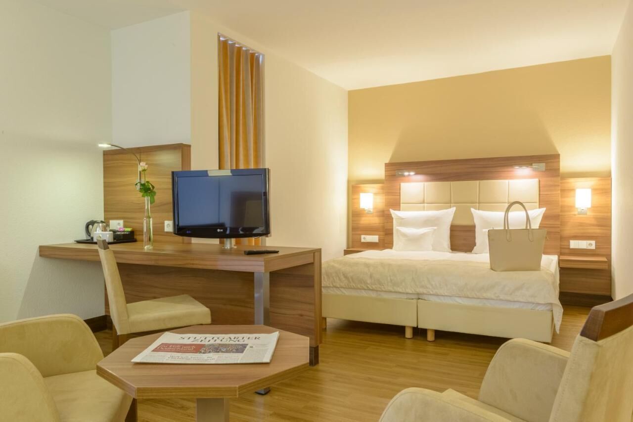 Une chambre d’hôtel avec un lit, un bureau avec une télévision, une chaise et une petite table sur laquelle repose un journal.