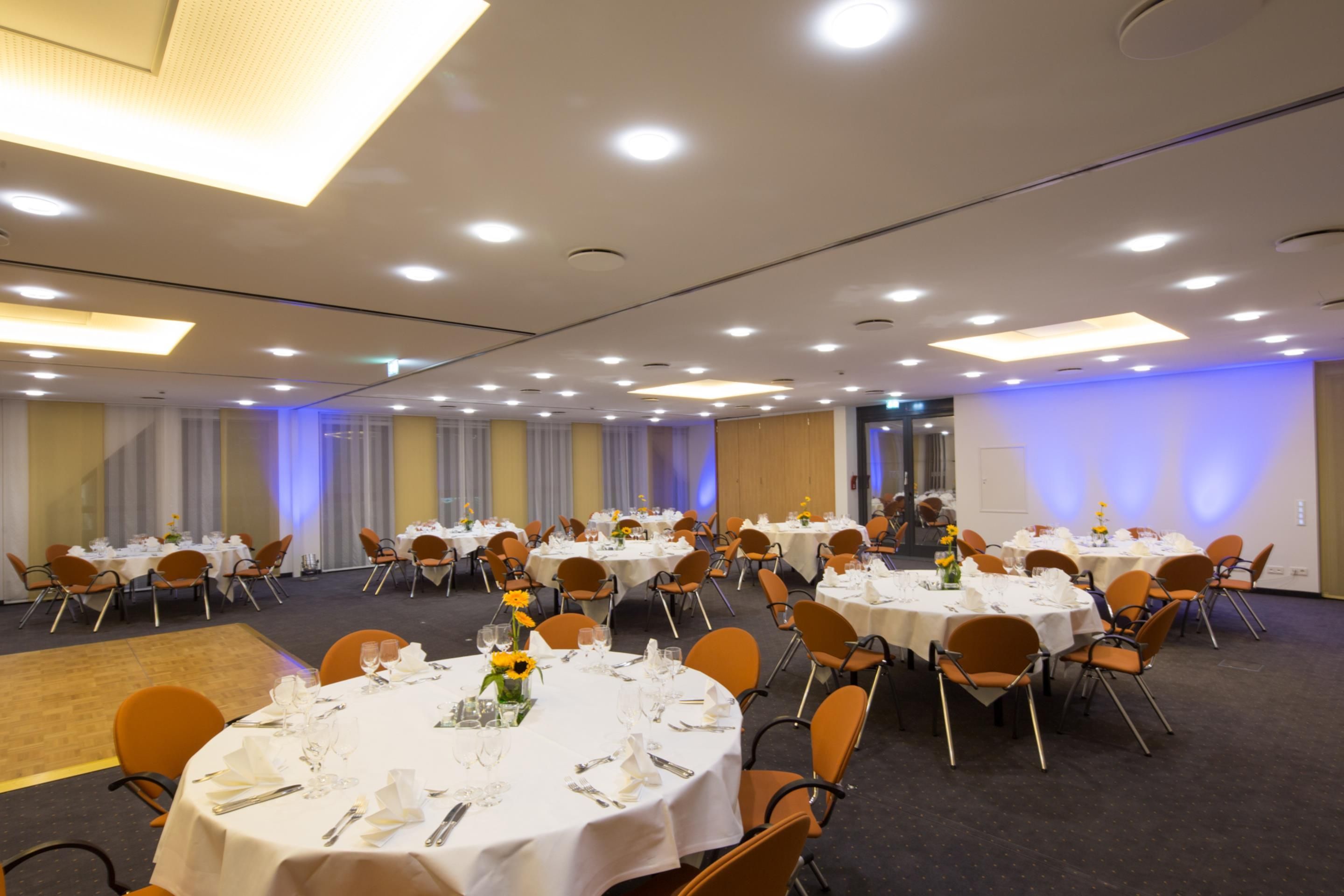 A conference room with round tables, chairs, and a carpeted floor.