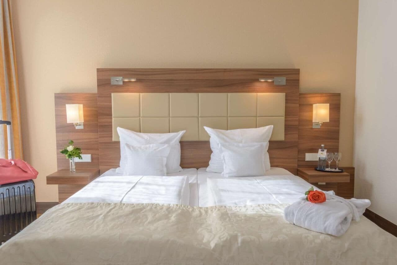 A hotel room with a large bed, two bedside tables, and a headboard with integrated lighting.