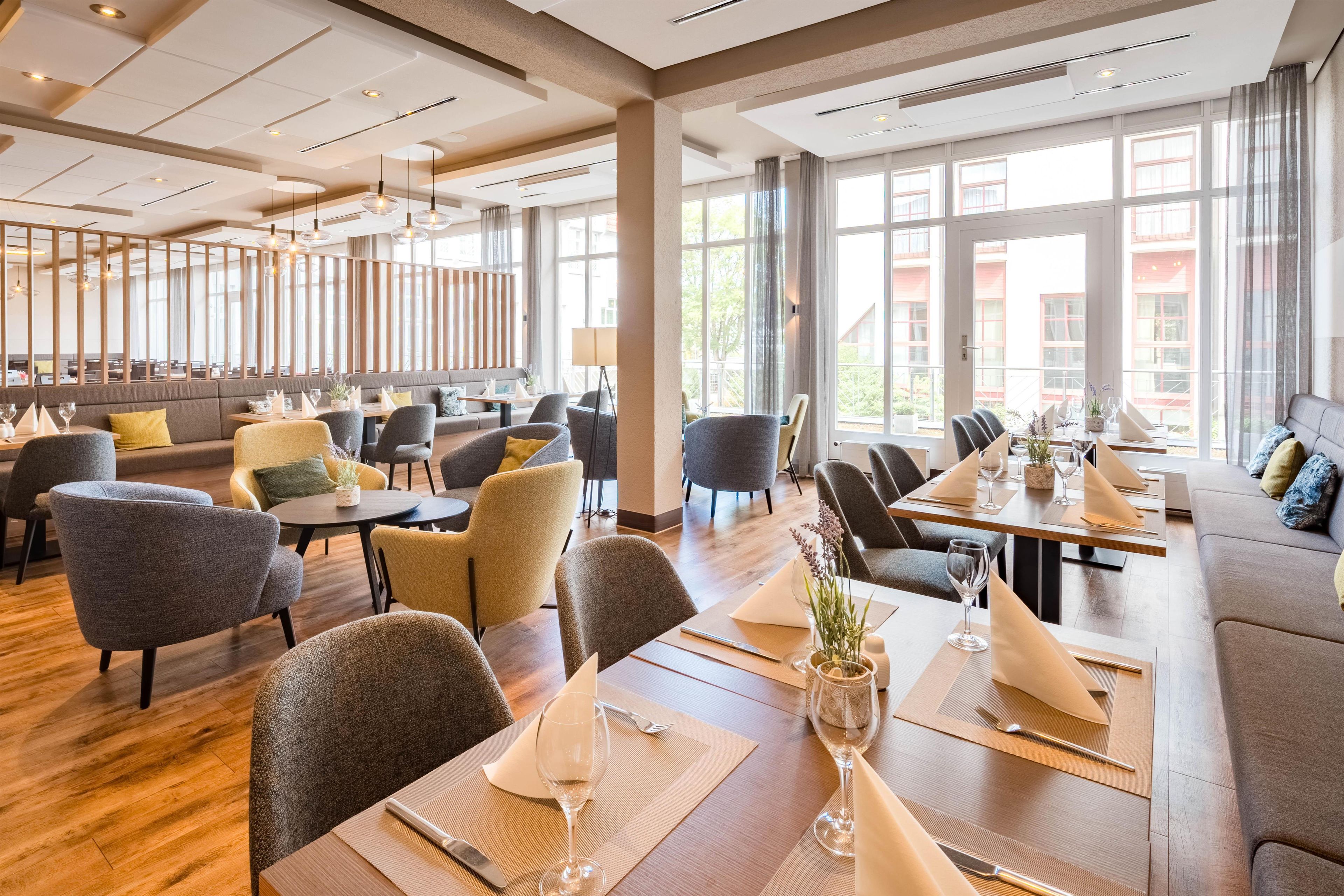 Um restaurante espaçoso com pé-direito alto, amplas janelas e diversas opções de assentos, incluindo mesas e sofás.