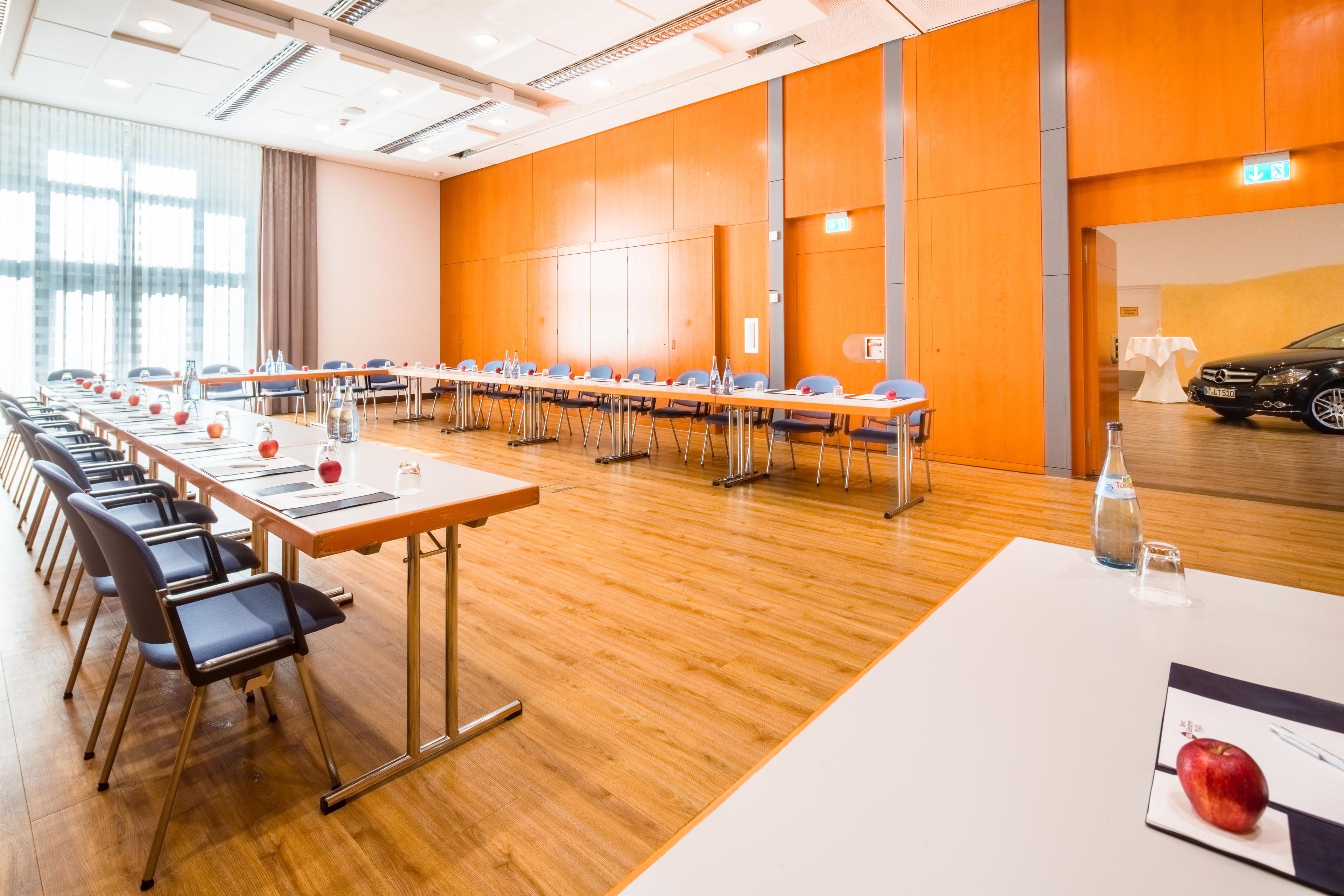 Une salle de conférence avec de longues tables, des chaises et une voiture garée à l’extérieur.