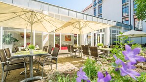 An outdoor patio with tables and chairs, large umbrellas, and a view of a building with large windows. - Best Western Plus Hotel Am Schlossberg (Nuertingen)