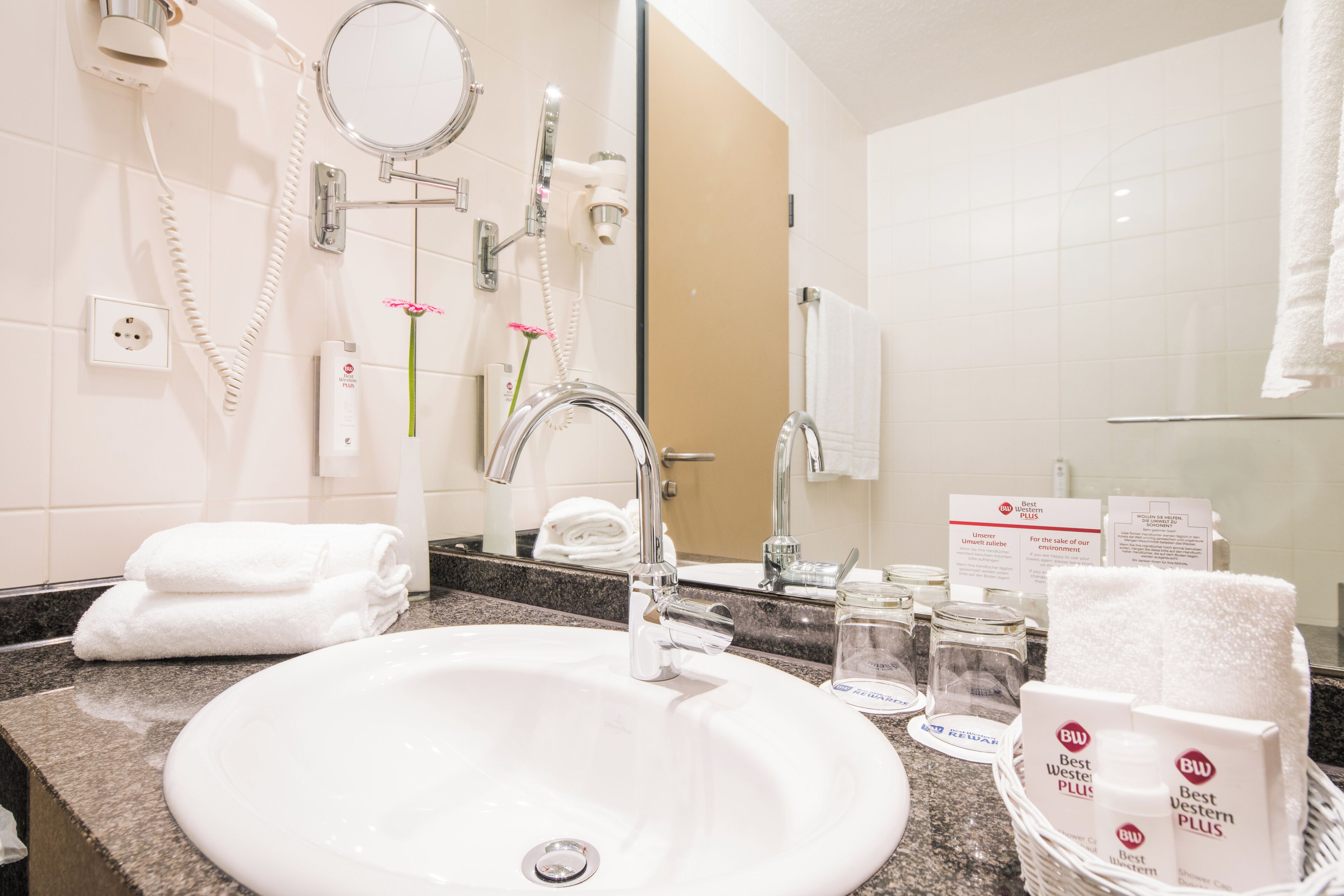 Un baño de hotel con lavamanos, espejo, toallero y cabina de ducha.