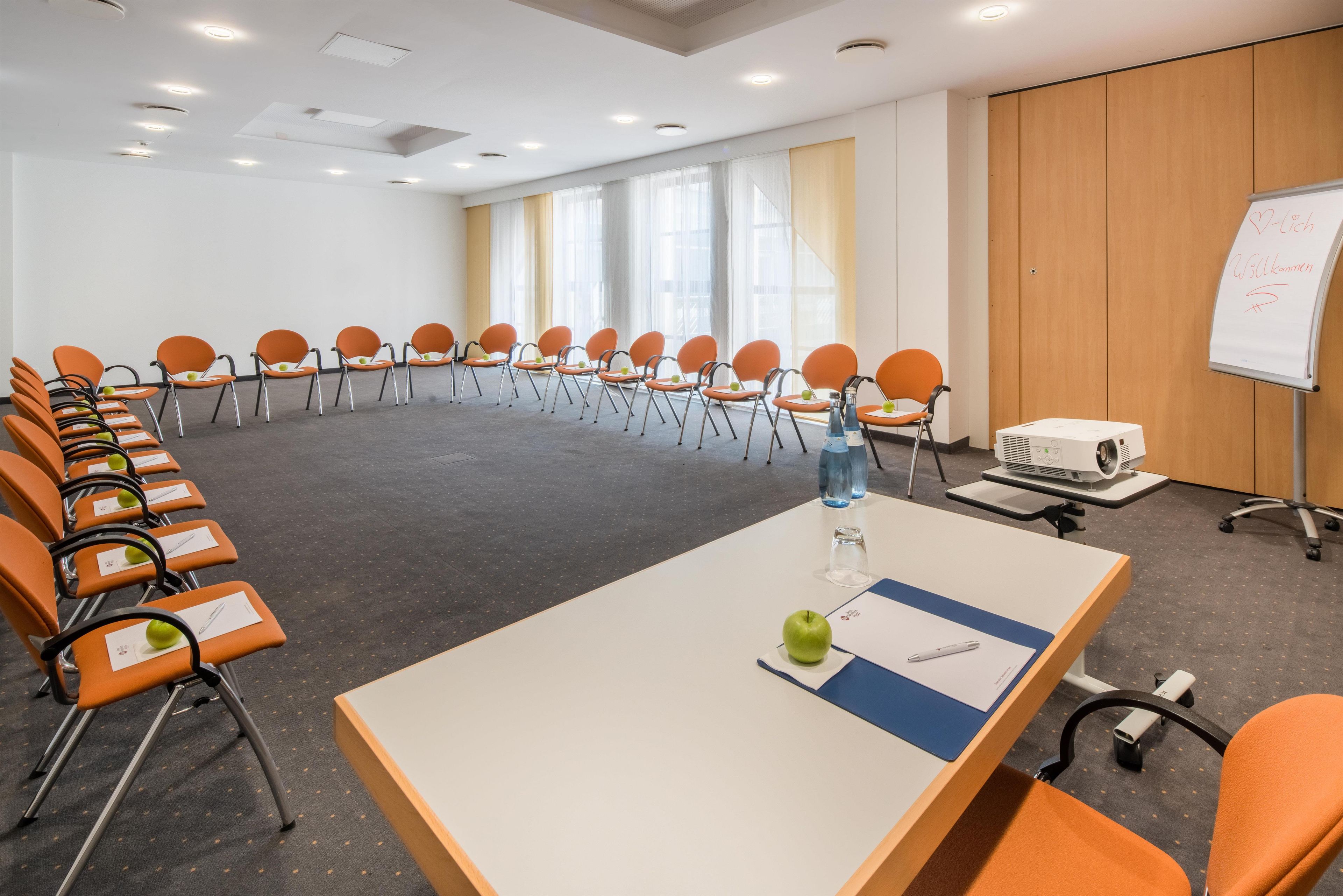 Un salón de conferencias con una larga mesa, varias sillas, una pizarra y un proyector.