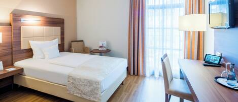 A hotel room with a bed, bedside table, lamp, desk, chair, and a TV.