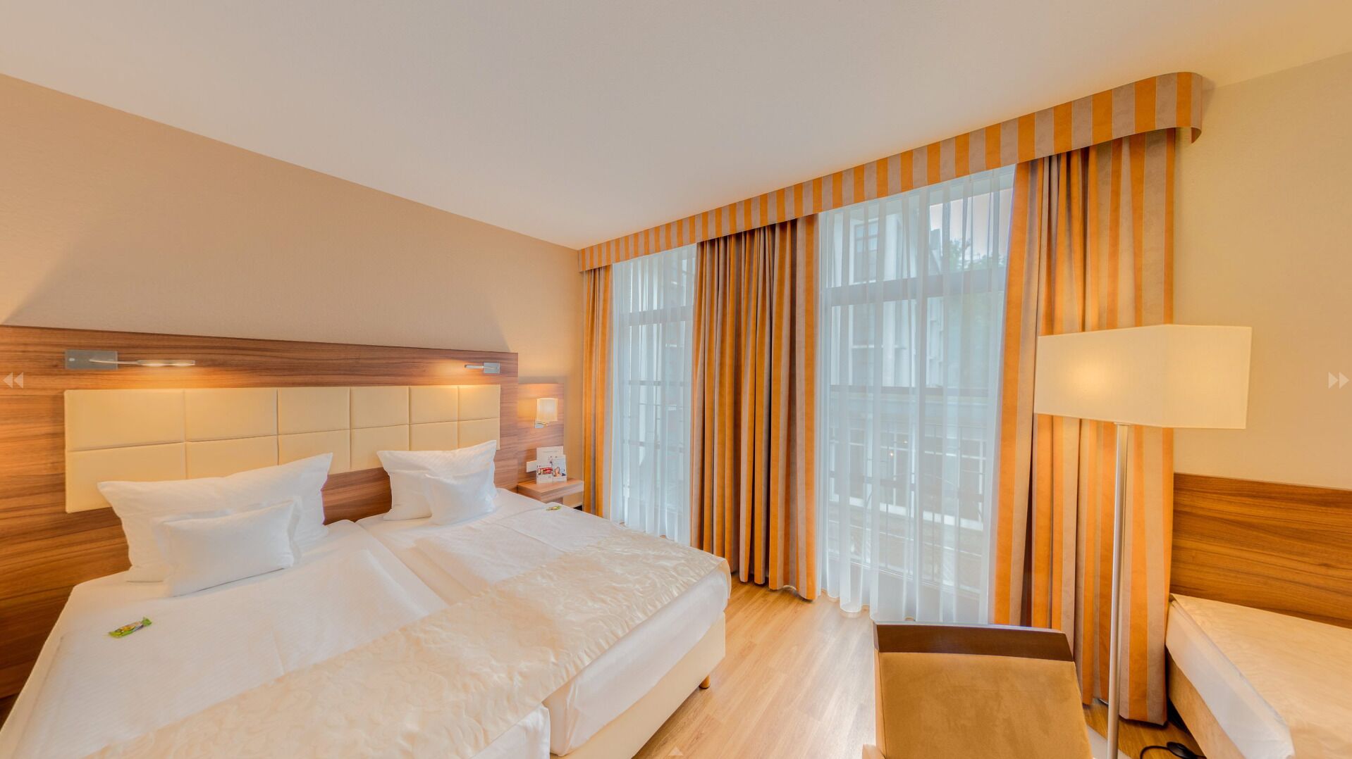 A hotel room with a large bed, a bedside table, a lamp, and a window with curtains.