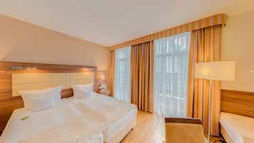 A hotel room with a large bed, a bedside table, a lamp, and a window with curtains.
