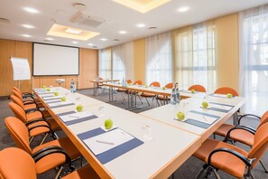 Een vergaderruimte met een lange tafel, stoelen, een projectiescherm en een whiteboard.