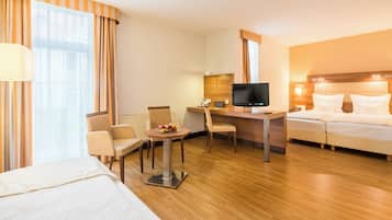A hotel room with a bed, a desk with a TV, a chair, and a small table with fruit.