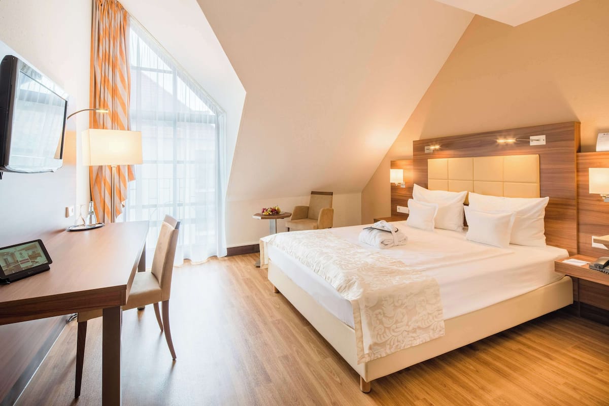 Habitación de hotel con una cama grande, un escritorio con silla, televisión y ventana con cortinas.